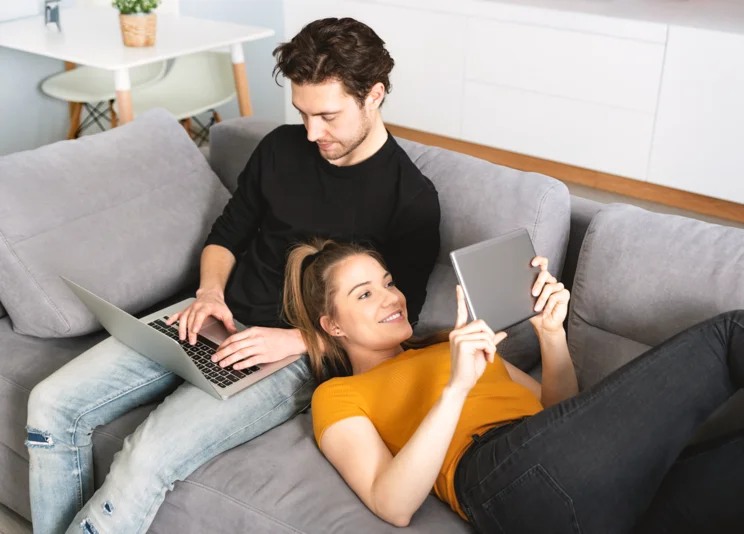 Frau und Mann auf Couch mit digitalen Geräten
